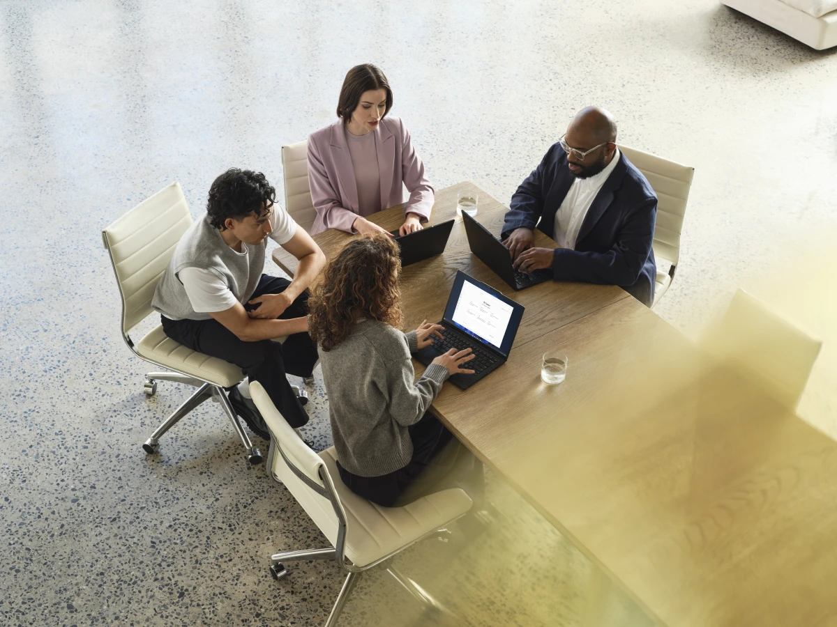 A group of people sitting around a table with laptops